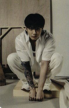 a young man kneeling down on top of a wooden floor next to a white wall