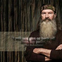 a man with a long beard wearing a camo hat and holding his arms crossed