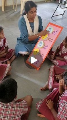 a group of children sitting on the floor in front of a woman holding a sign