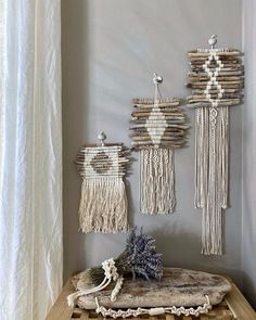 three wall hangings made out of driftwood and rope on a table in front of a window