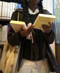 a woman standing in front of a bookshelf holding two open book's