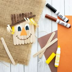 popsicle scarecrow craft with supplies to make it on white wood boards and burlap