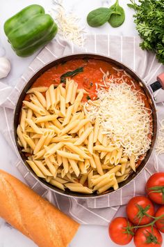 a pan filled with pasta and sauce next to tomatoes, parmesan cheese and green peppers