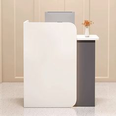 a white and grey desk with a flower vase on the top, next to it