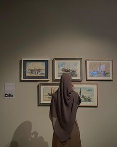 a woman in a hijab looking at pictures on the wall