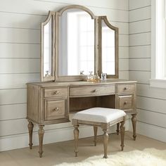 an antique vanity with mirror and stool in a white room