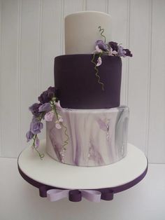 a three tiered cake with purple and white decorations on the top is decorated with flowers