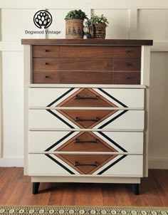 a white dresser with brown and black geometric designs on it's drawers next to a potted plant