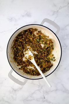 a pot filled with food sitting on top of a white marble counter next to a spoon