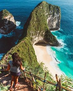 a woman walking up the stairs to an island with two large rocks in the water