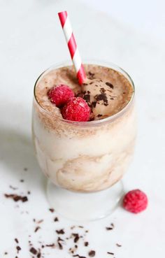 a glass filled with ice cream and raspberries on top of a white table