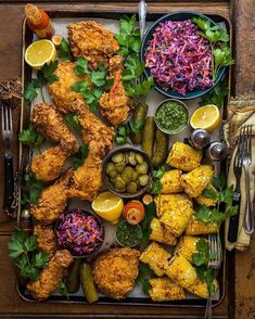 a platter filled with chicken, coleslaw and pickles next to other foods