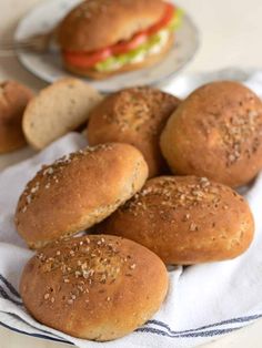 rolls with sesame seeds are on a white towel next to a plate of burgers