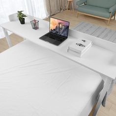 an open laptop computer sitting on top of a white table next to a book and plant