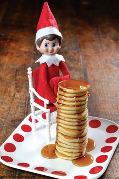 an elf is sitting on a chair next to stack of pancakes