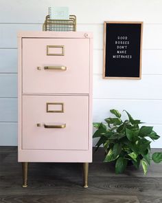 a pink filing cabinet next to a potted plant and a chalkboard on the wall