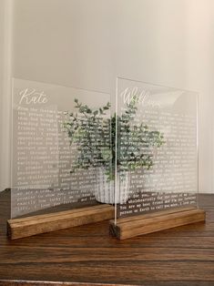 two clear acrylic vases with plants in them sitting on a wooden table