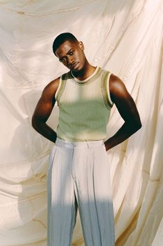 a man standing with his hands on his hips wearing white pants and a green tank top