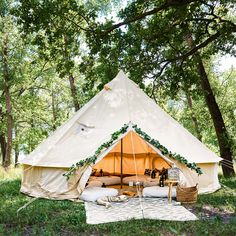 a teepee tent with pillows and blankets in the grass next to it, surrounded by trees