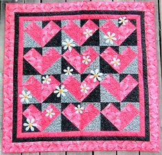 a pink and black quilt with white flowers on the center is sitting on a wooden surface