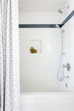 a white bath tub sitting under a window next to a shower head mounted on a wall