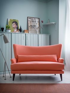 an orange couch sitting on top of a wooden floor next to a lamp and dresser