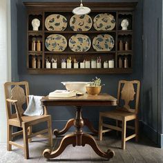 a dining room table with two chairs and plates on the wall above it, in front of an open bookcase