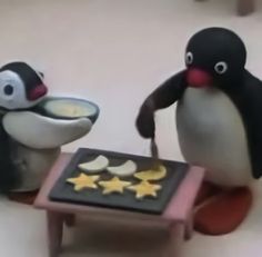 two penguins are standing next to each other and one penguin is eating from a plate