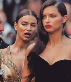 two beautiful women standing next to each other in front of a man wearing a suit