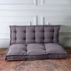 a gray futon couch sitting on top of a rug in front of a white wall