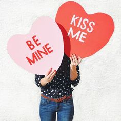 a woman holding two heart shaped signs with the words be mine and kiss me on them