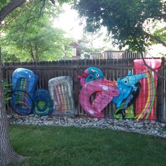 a fence that has some type of art on it in front of a tree and grass area