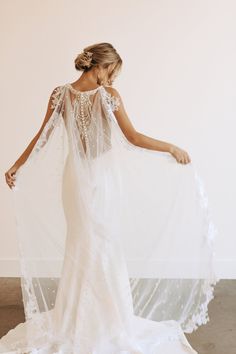 a woman in a white wedding dress with a veil on her head and back, standing against a wall