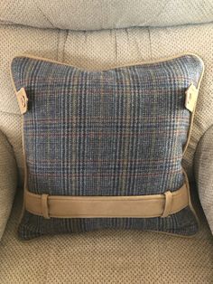 a blue plaid pillow sitting on top of a couch next to a brown leather belt