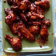 chicken wings with sauce on a green plate next to two blue plates filled with bread