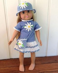 a doll wearing a blue dress and hat with white daisies on the bottom, standing in front of a door