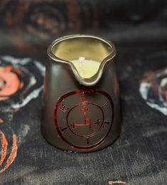 a candle that is sitting in a cup on a tablecloth with an orange and black design