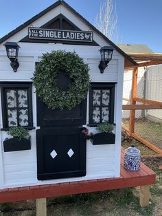 a small white house with black shutters and a wreath on the door, sitting in front of a fence