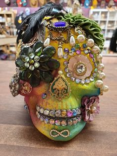 a colorful skull with flowers and feathers on it's head sitting on a table