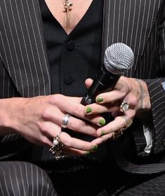 a man in a suit holding a microphone and wearing green nail polish on his nails