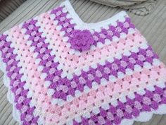 a pink and white crocheted blanket sitting on top of a wooden floor next to a pair of shoes