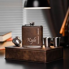 a flask and shot glasses sitting on a desk next to a lighter with the name kyyle written on it