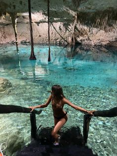 a woman in a bathing suit standing at the edge of a pool with clear blue water