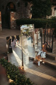 a couple of mirrors sitting on the side of a building next to flowers and plants