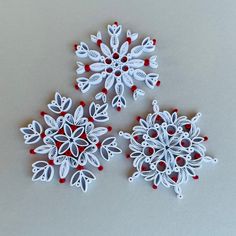 three white snowflakes with red and white decorations on the top one is made out of paper