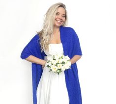 a woman in a white dress and blue cardigan is holding a bouquet of flowers