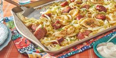 a casserole dish with sausage, onions and cabbage on a colorful table cloth