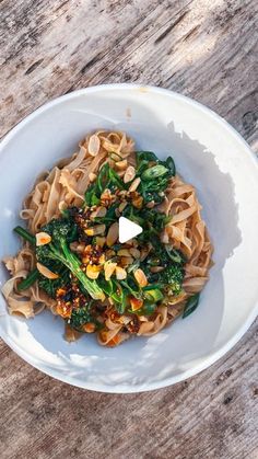 a white bowl filled with pasta and broccoli on top of a wooden table