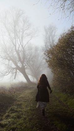 a woman walking down a path in the fog