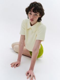 This piece of clothing is a short-sleeved knitted top with a textured pattern. It features a prominent collar with a single button fastening at the neck. The fit is snug around the waist and loose around the shoulders and chest. The sleeves end above the elbow with a soft, ribbed finish.- The garment displays a classic collar design, enhancing its structured neckline.- It has a cropped cut, sitting just above the waist, revealing the midriff slightly.- A single pearlescent button adds a subtle decorative element while serving as a functional closure at the throat. Knitted Top, Collar Designs, Piece Of Clothing, Ice Cream, Cream, Collar, Knitting, Pattern, Clothes